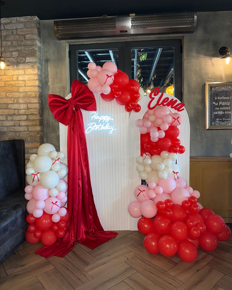 Beli lukovi sa velikom crvenom satenskom mašnom, svetlećim natpisom Happy Birthday i crveno roze balonima