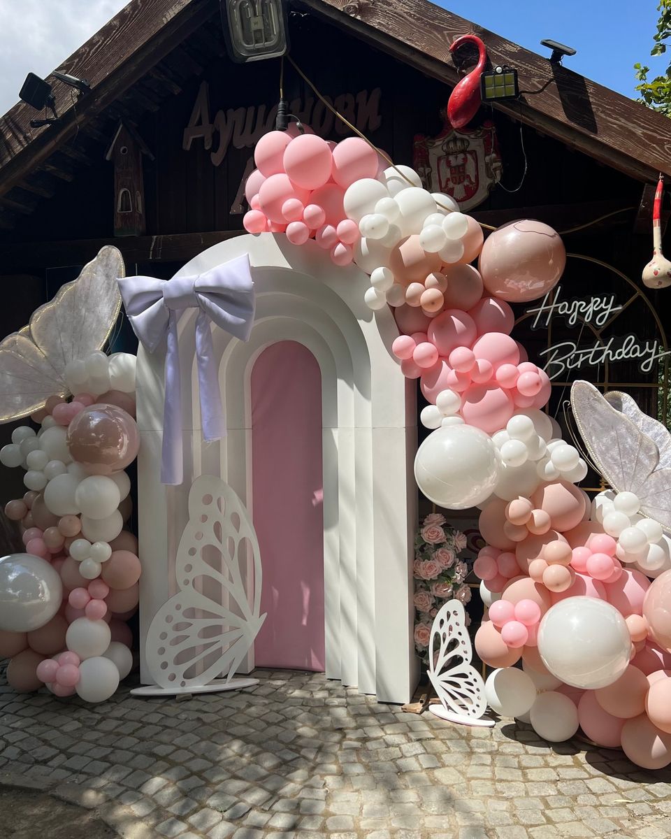 Beli stepenasti luk sa roze vratima, beli leptiri, roze i beli baloni i lila mašna