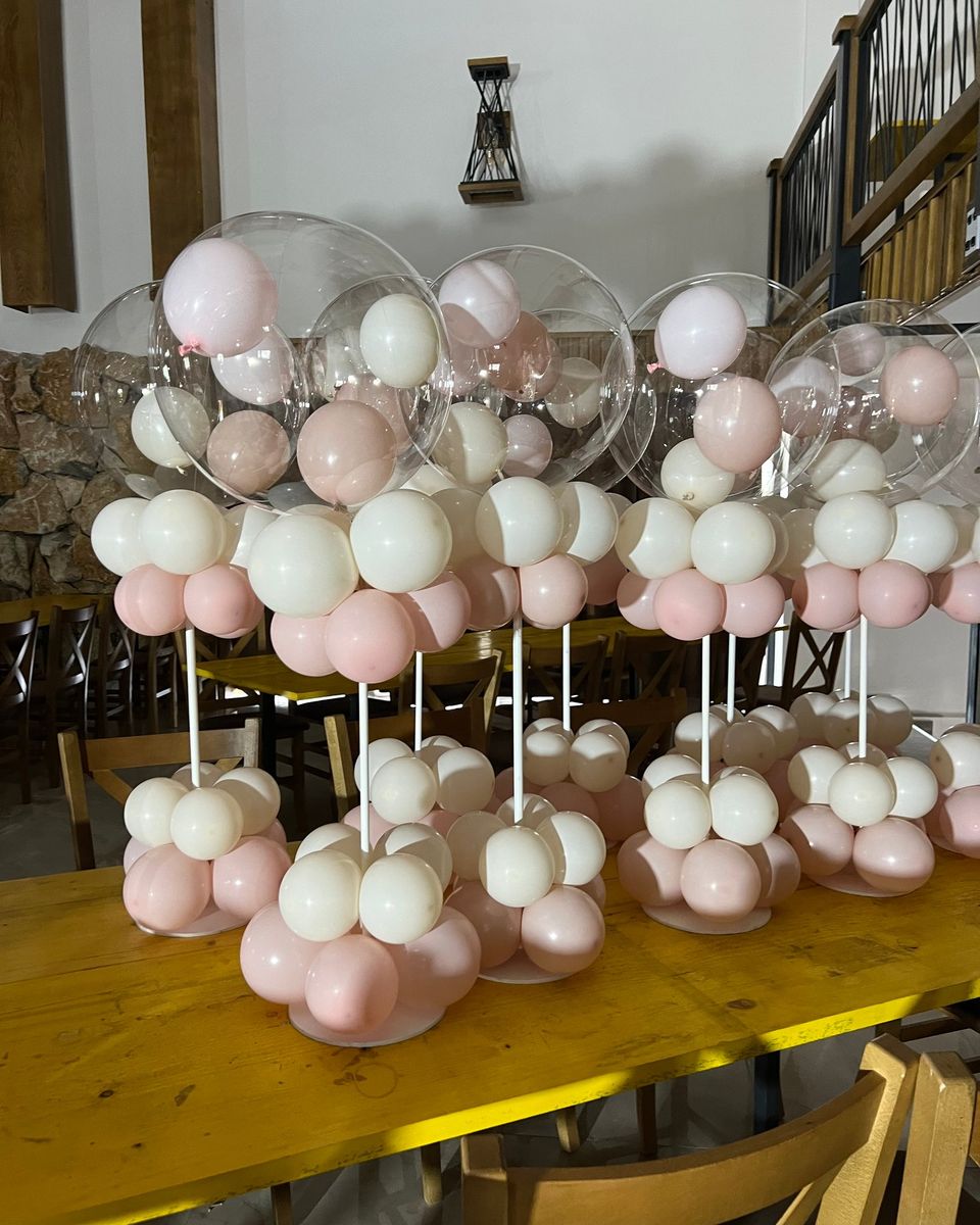 Više stonih dekoracija sa providnim balonima i roze i belim balonima na stolu