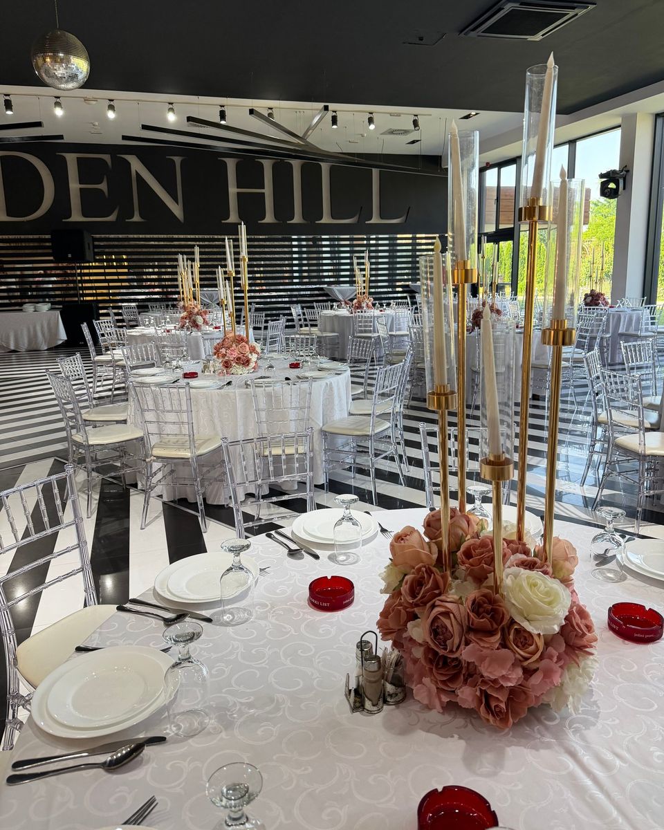 Zlatni svećnjaci sa staklenim cilindrima i puder roze ruže na okruglom stolu