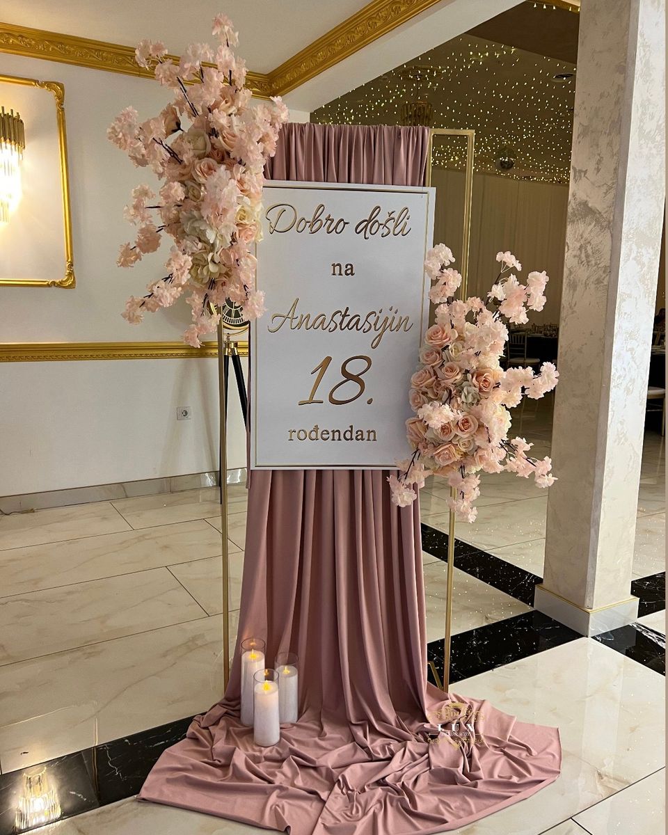 Tabla dobrodošlice za 18. rođendan sa starinsko roze draperijom, roze cvećem i svećama