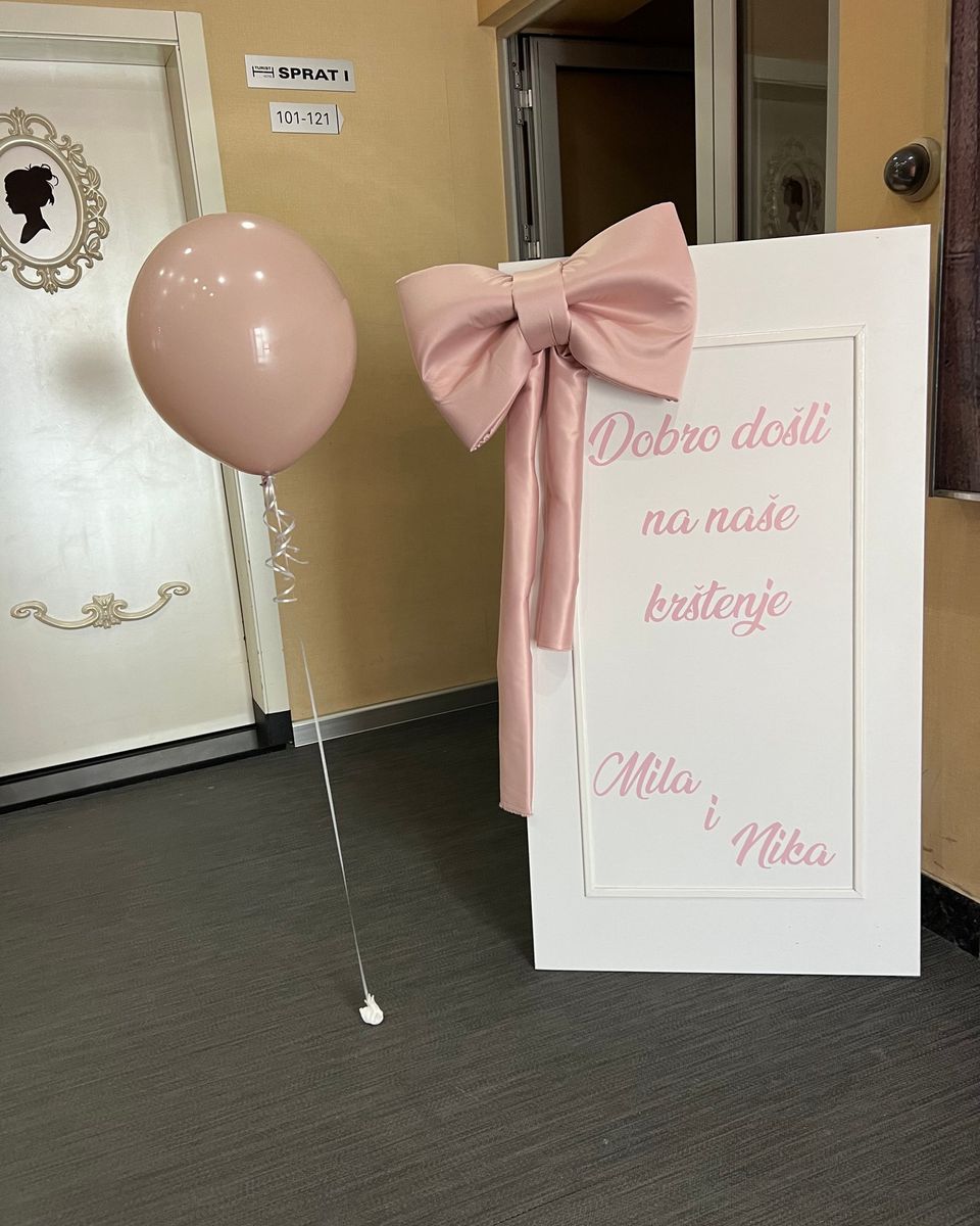 Beli pano za krštenje sa roze slovima, roze mašnom i jednim velikim balonom