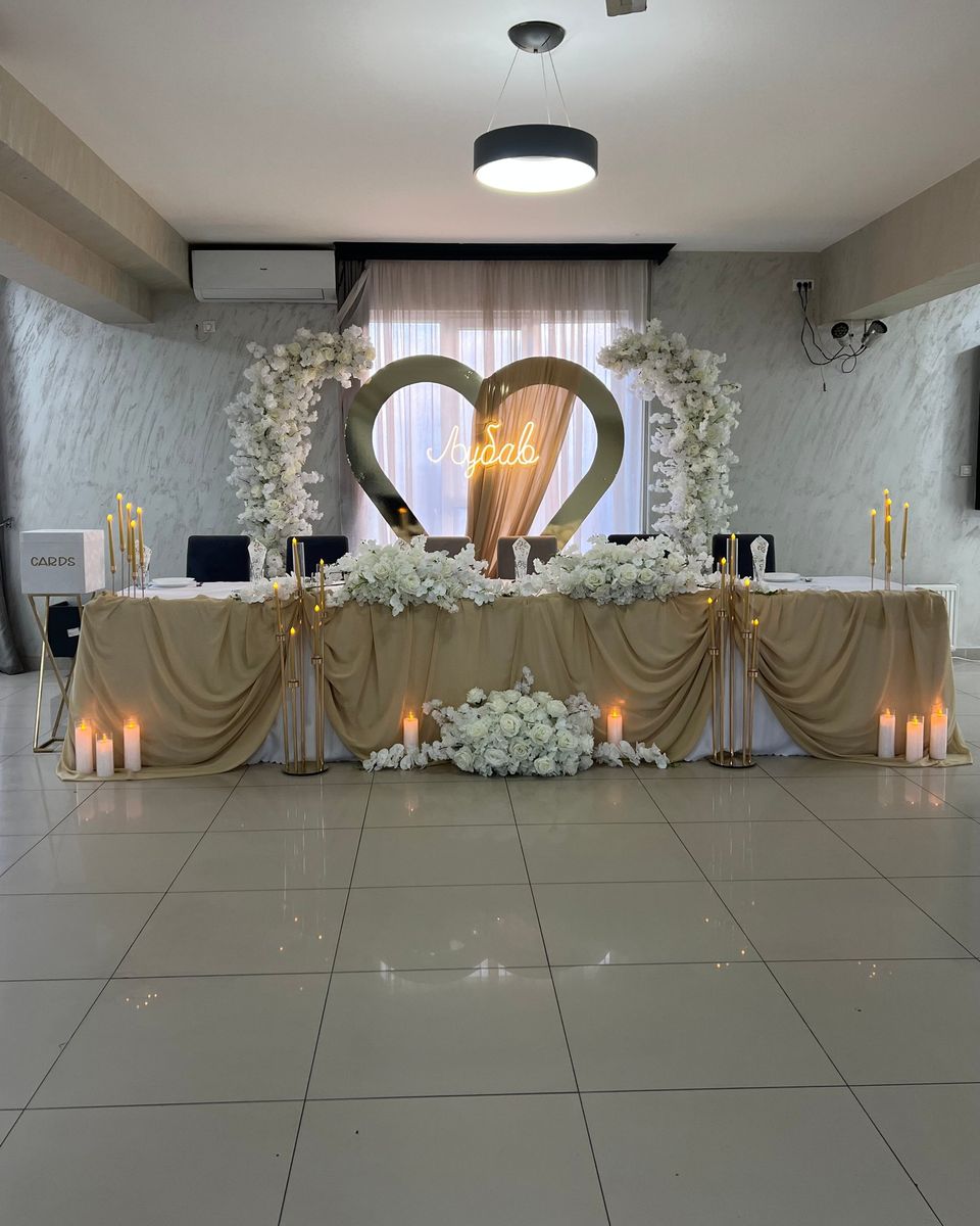 Glavni sto sa šampanj draperijom, svećama i zlatnim srcem sa natpisom Ljubav između lukova